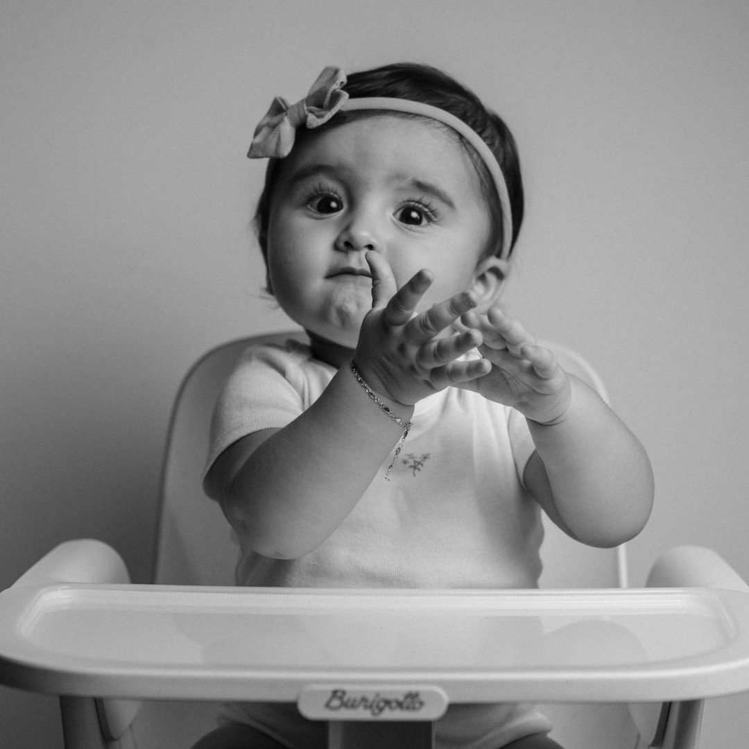 Ein Kleinkind im Hochstuhl, das mit Händen spielt und lächelt und auf sein Essen wartet.