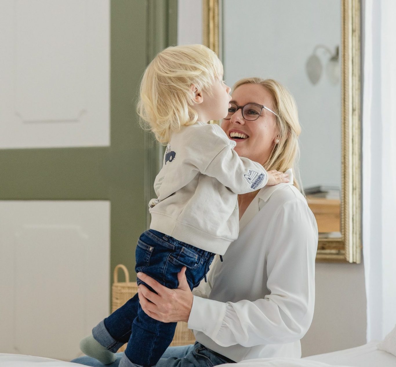 Ein lachender Junge umarmt seine Mutter, die glücklich auf einem Bett sitzt.